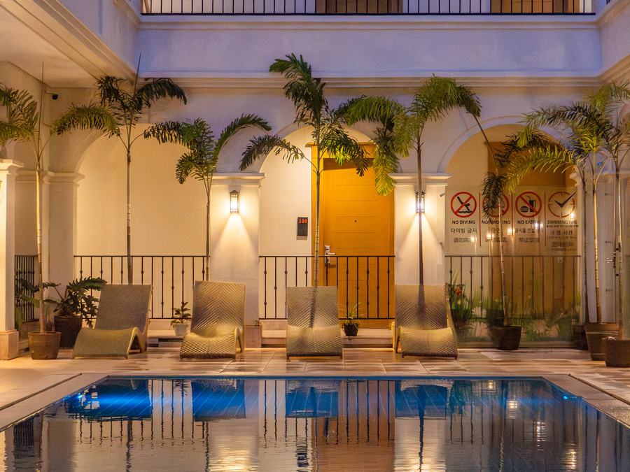 The pool courtyard at Boracay Sands: loungers along a lit colonnade with arched doorways and potted palms, reflected in the water.