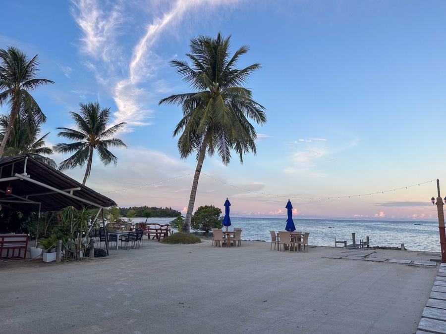 Reef Beach Resort's beachfront in General Luna: coconut palms, umbrellas and tables on the sand above the sea.