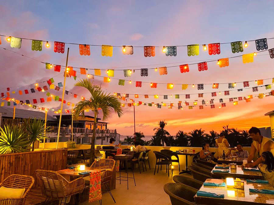 Salsa Fusion, Serene La Playa's rooftop restaurant, at sunset: tables beneath strings of coloured bunting, with palms beyond.