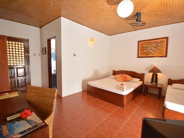 Classic Room at Hibiscus Garden: a queen bed and a single bed on terracotta tiles beneath a woven bamboo ceiling.