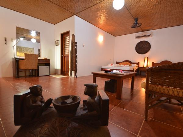 Family Room at Hibiscus Garden: two queen beds on terracotta tiles with carved timber furniture and a woven ceiling.