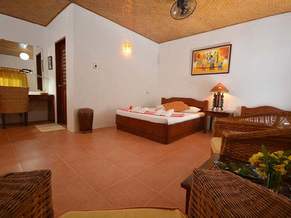 Queen Room at Hibiscus Garden: queen bed with a single beside it, rattan chairs and a table by the window.