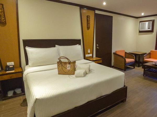 Classic Room at Red Coconut: queen bed with white linens under a dark timber headboard, with a seating corner by the window.