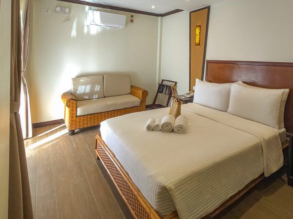 Deluxe Pool View at Red Coconut: king bed with white linens, a rattan sofa and armchair beside it on timber floors.