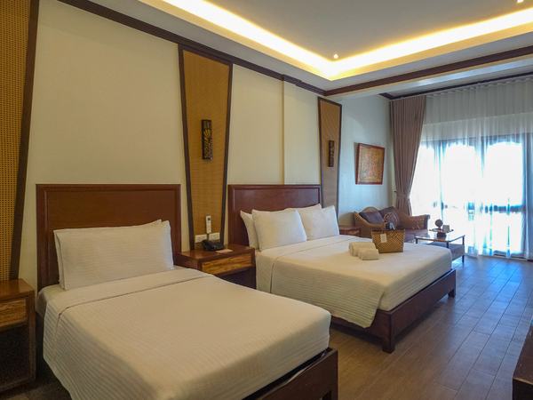Premier Beach View at Red Coconut: two double beds under a carved timber headboard, balcony doors open to the light.
