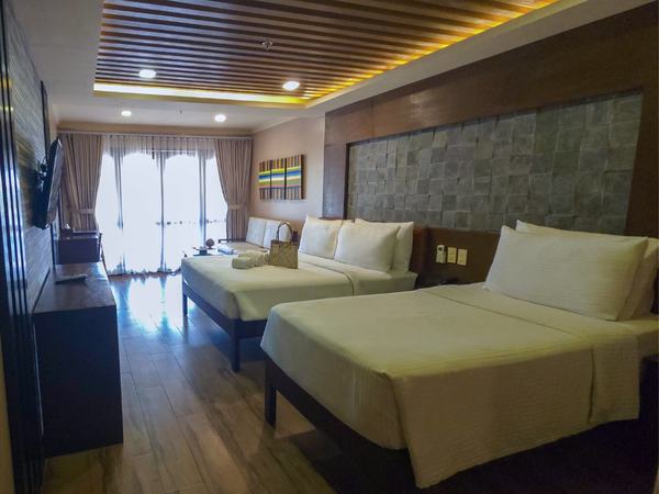 Premier Pool View at Red Coconut: two beds with green throws against a stone feature wall, balcony doors to one side.