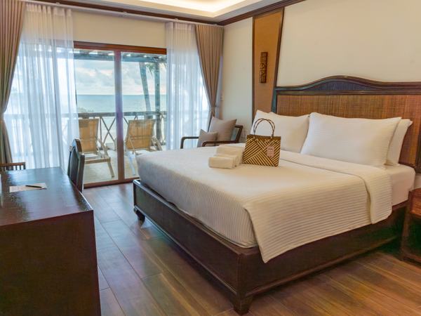 Presidential Suite at Red Coconut: king bed with a rattan armchair and desk, sliding doors to a private balcony.