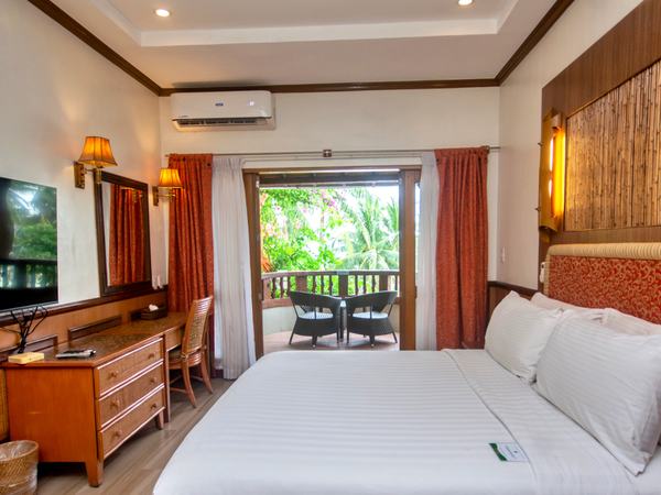 Suite Beach View at Red Coconut: king bed facing a timber dresser and mirror, with balcony doors open onto greenery.