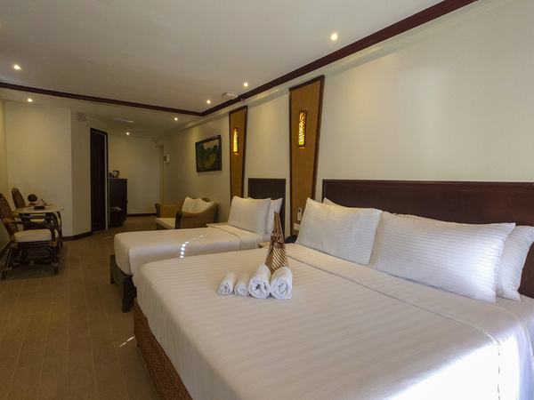 Suite Pool View at Red Coconut: two double beds with towel swans, a seating area beyond and warm timber panelling.