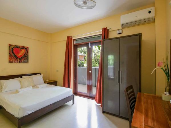 One Bedroom Suite at Reef Beach Resort: king bed with red curtains, a wardrobe and balcony doors to the garden.