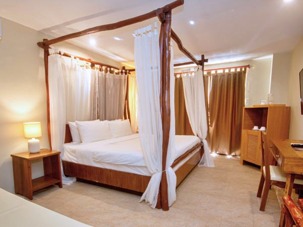 Grand Oasis at Serene La Playa: four-poster king bed with draped white curtains and a seating area beyond.